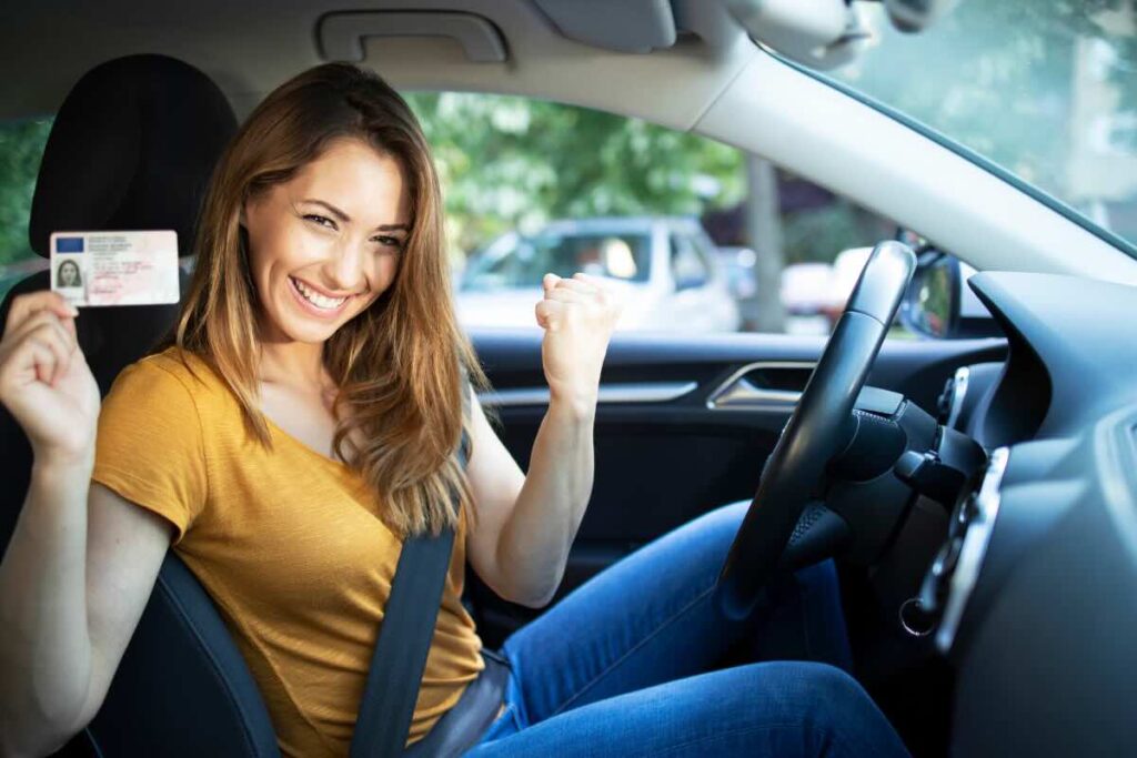 ragazza felice in auto con cintura di sicurezza e patente in mano